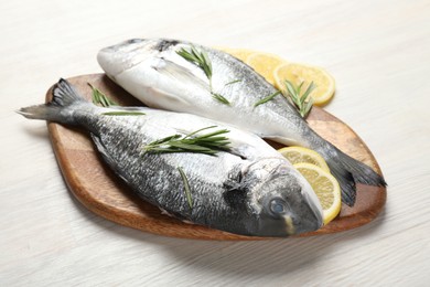 Photo of Fresh raw dourade fish, lemon slices and rosemary on white wooden table, closeup. Organic seafood