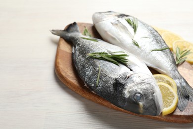 Photo of Organic seafood. Fresh raw dourade fish, lemon slices and rosemary on white wooden table, closeup. Space for text