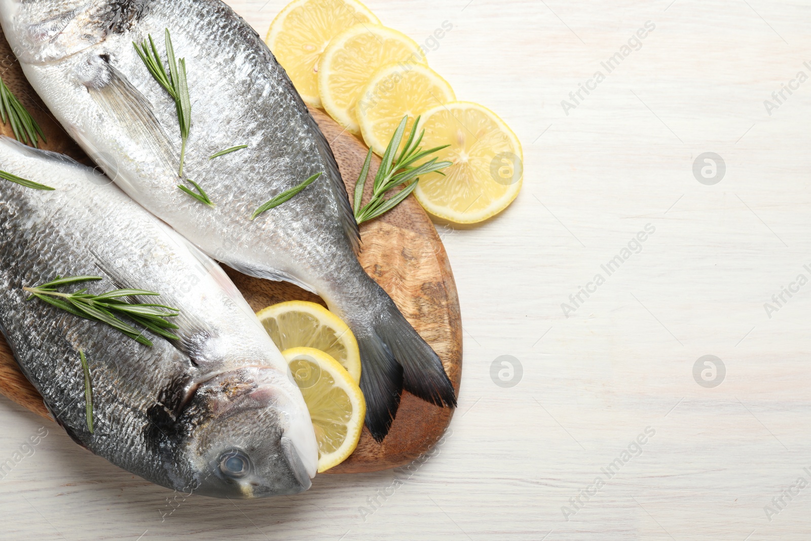 Organic seafood. Fresh raw dourade fish, lemon slices and rosemary on white wooden table, flat lay. Space for text Photo of Organic seafood. Fresh raw dourade fish, lemon slices and rosemary on white wooden table, flat lay. Space for text