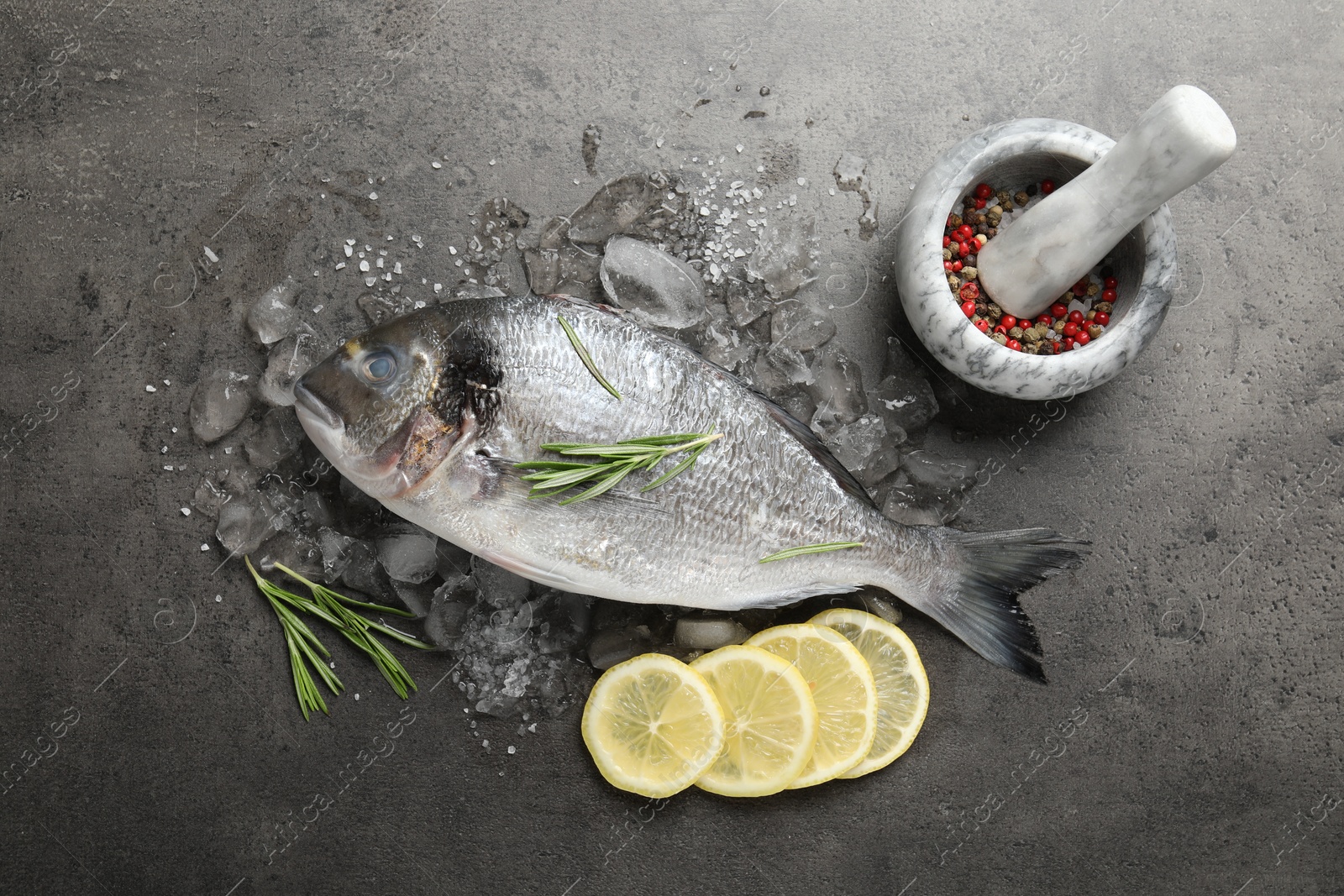Fresh raw dourade fish, ice, lemon slices and rosemary on grey table, flat lay. Organic seafood Photo of Fresh raw dourade fish, ice, lemon slices and rosemary on grey table, flat lay. Organic seafood