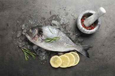 Photo of Fresh raw dourade fish, ice, lemon slices and rosemary on grey table, flat lay. Organic seafood