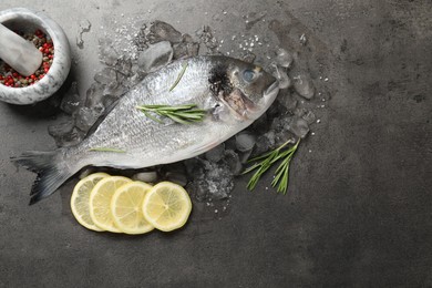 Photo of Organic seafood. Fresh raw dourade fish, ice, lemon slices and rosemary on grey table, flat lay. Space for text