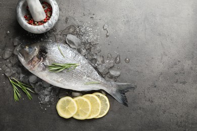 Photo of Organic seafood. Fresh raw dourade fish, ice, lemon slices and rosemary on grey table, flat lay. Space for text