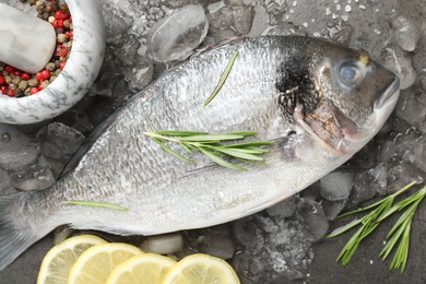 Photo of Fresh raw dourade fish, ice, lemon slices and rosemary on grey table, flat lay. Organic seafood