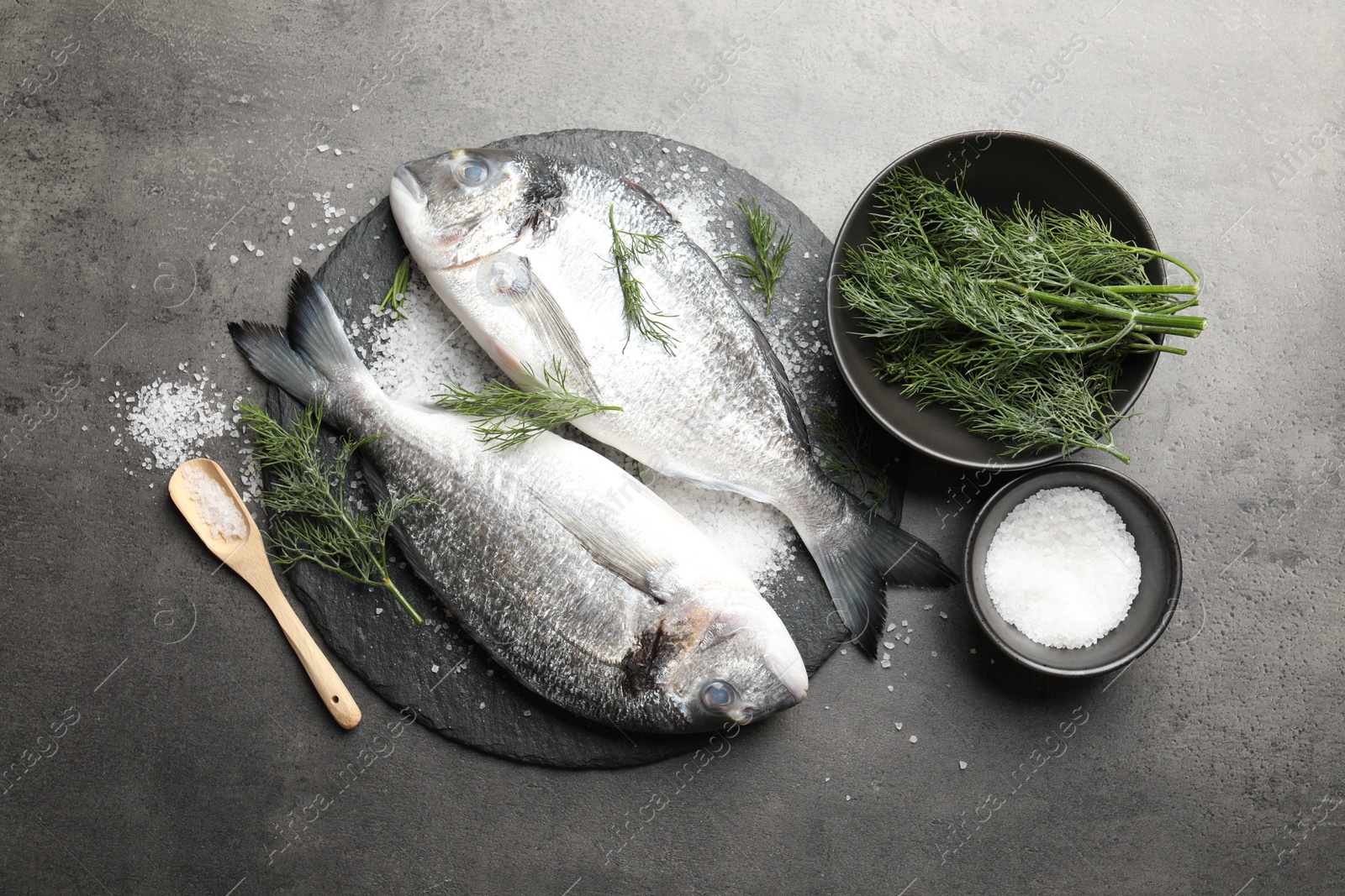 Organic seafood. Fresh raw dourade fish, salt and dill on grey table, flat lay Photo of Organic seafood. Fresh raw dourade fish, salt and dill on grey table, flat lay
