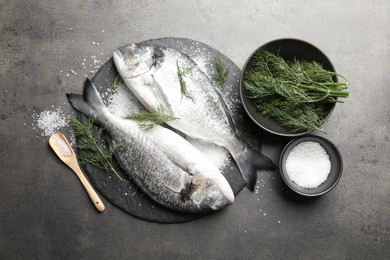 Photo of Organic seafood. Fresh raw dourade fish, salt and dill on grey table, flat lay
