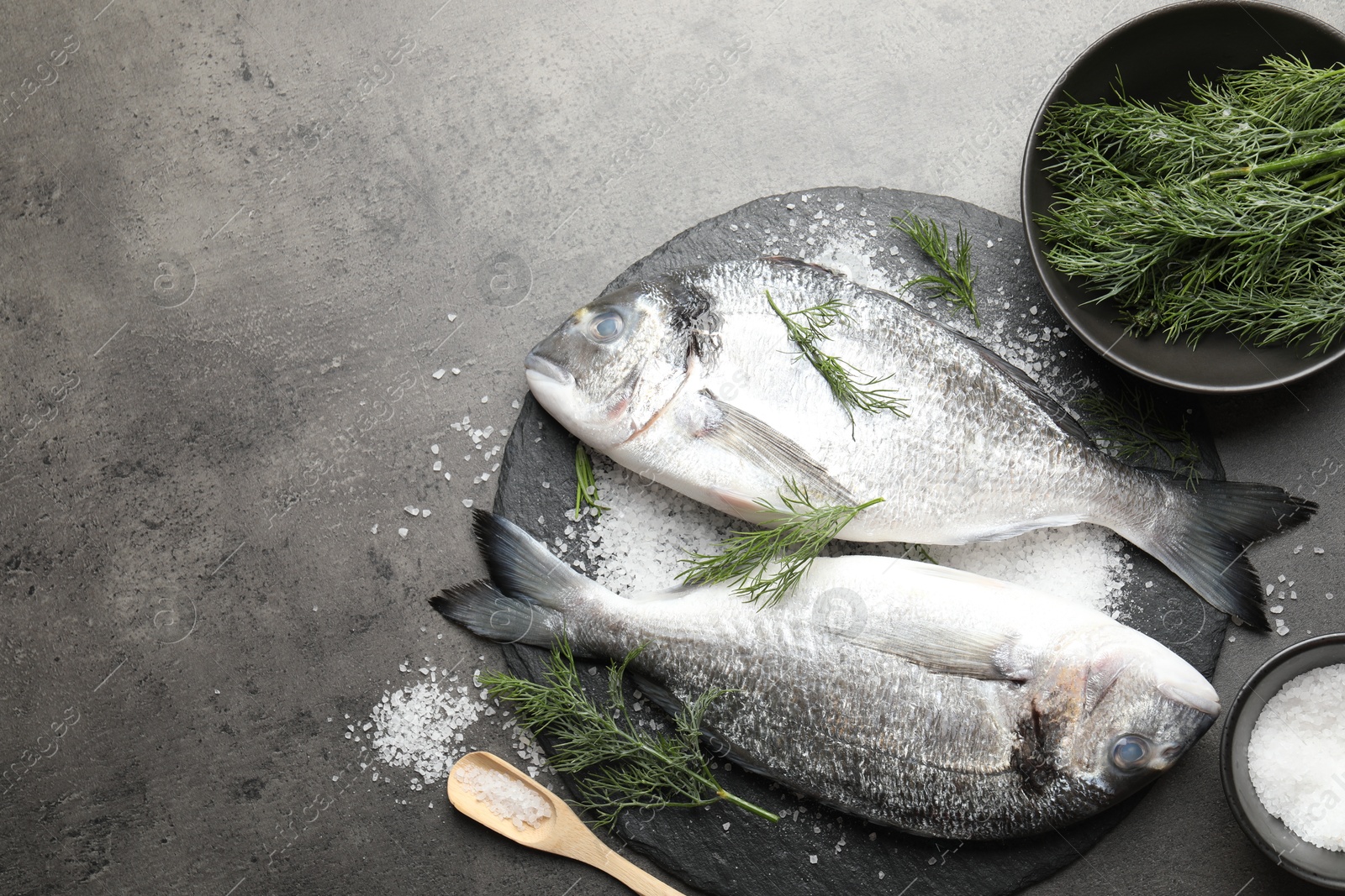 Organic seafood. Fresh raw dourade fish, salt and dill on grey table, flat lay. Space for text Photo of Organic seafood. Fresh raw dourade fish, salt and dill on grey table, flat lay. Space for text