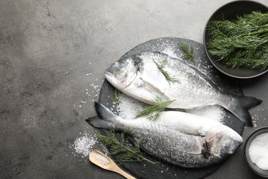 Photo of Organic seafood. Fresh raw dourade fish, salt and dill on grey table, flat lay. Space for text