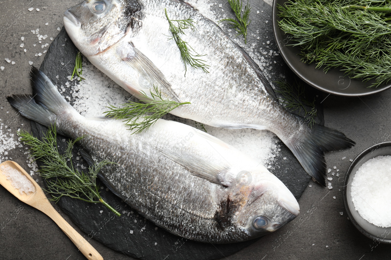 Photo of Organic seafood. Fresh raw dourade fish, salt and dill on grey table, flat lay