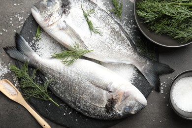 Photo of Organic seafood. Fresh raw dourade fish, salt and dill on grey table, flat lay