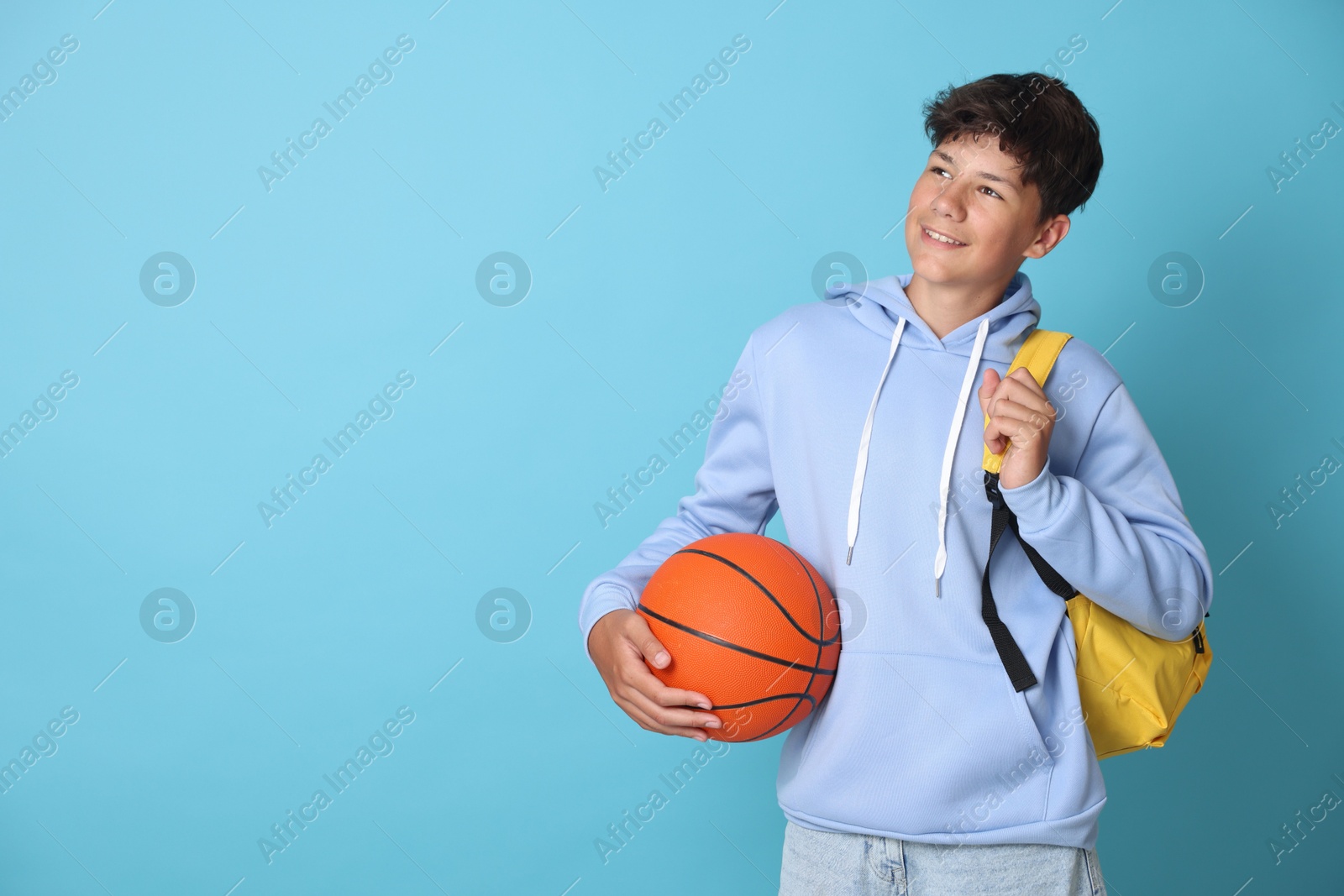 Photo of Teenage boy with backpack and basketball ball on light blue background, space for text