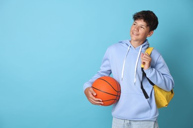 Photo of Teenage boy with backpack and basketball ball on light blue background, space for text