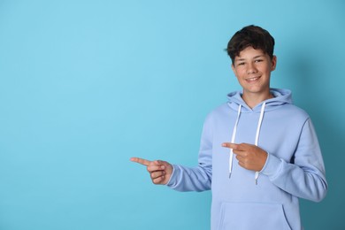 Photo of Teenage boy pointing at something on light blue background, space for text