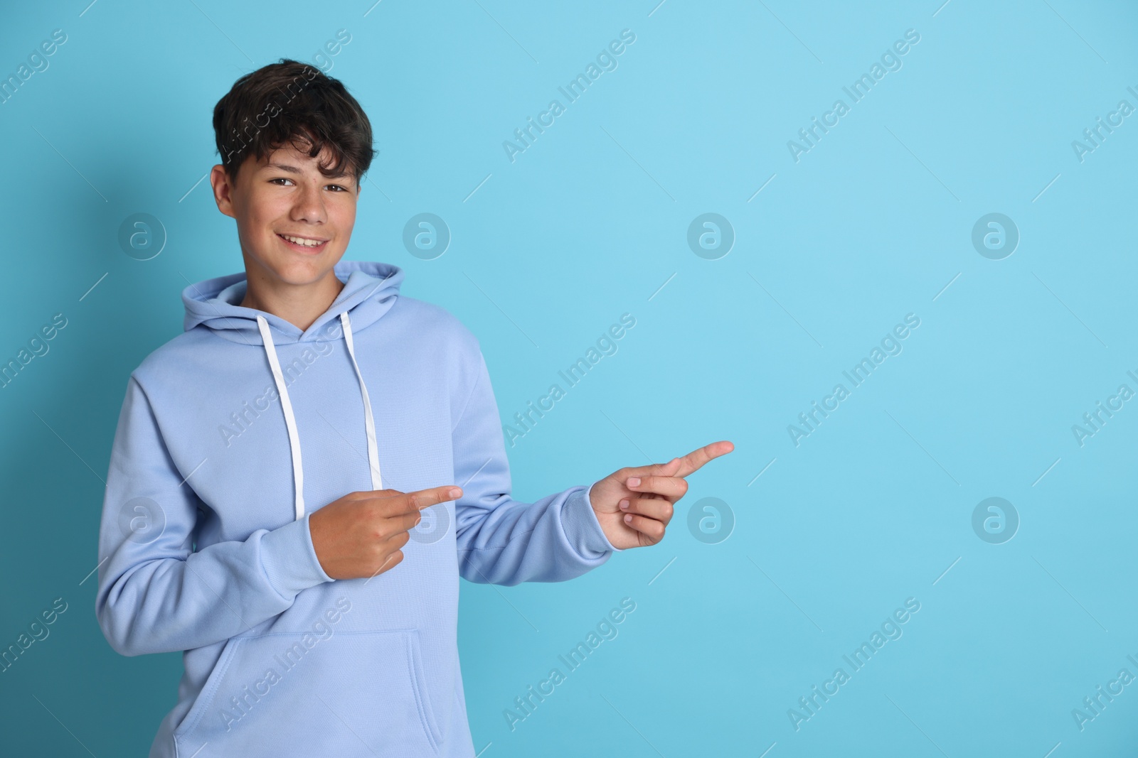 Teenage boy pointing at something on light blue background, space for text Photo of Teenage boy pointing at something on light blue background, space for text