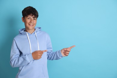 Photo of Teenage boy pointing at something on light blue background, space for text