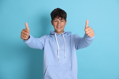 Photo of Teenage boy showing thumbs up on light blue background