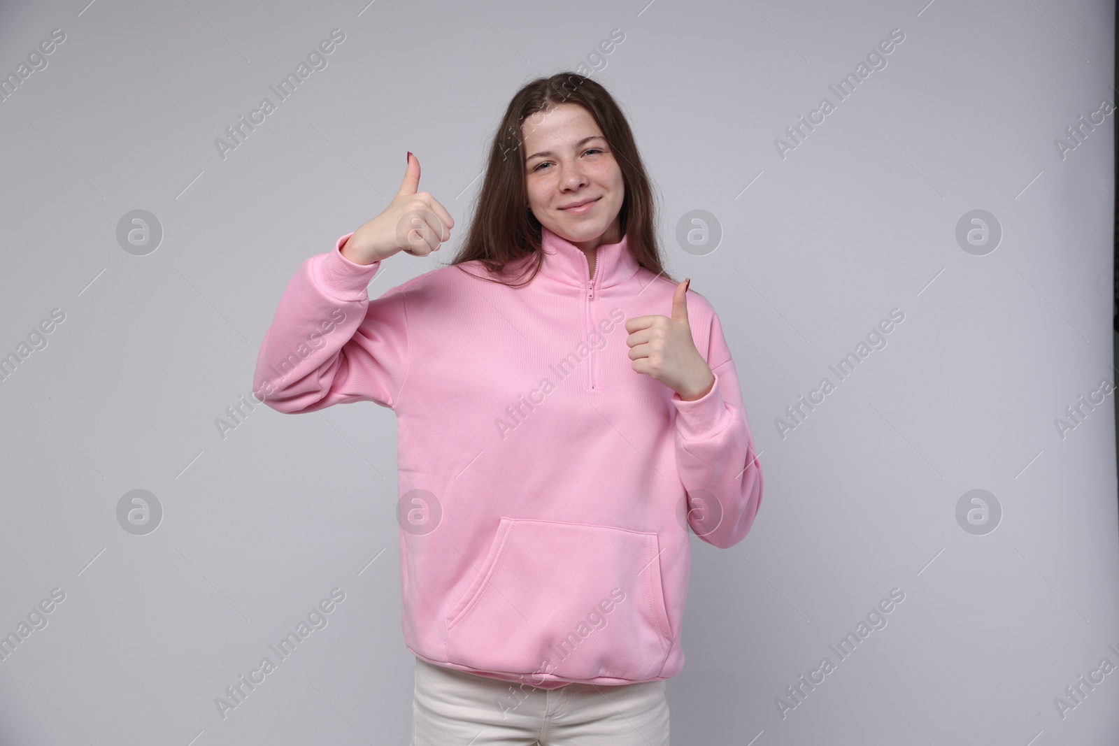 Teenage girl showing thumbs up on light grey background Photo of Teenage girl showing thumbs up on light grey background