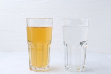 Photo of Glasses with clean and dirty water on white tiled table
