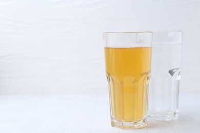 Photo of Glasses with clean and dirty water on white tiled table, closeup. Space for text