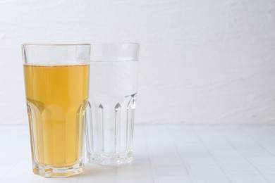 Photo of Glasses with clean and dirty water on white tiled table, closeup. Space for text