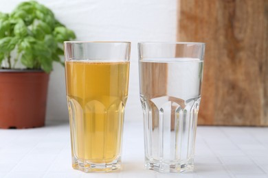 Photo of Glasses with clean and dirty water on white tiled table, closeup