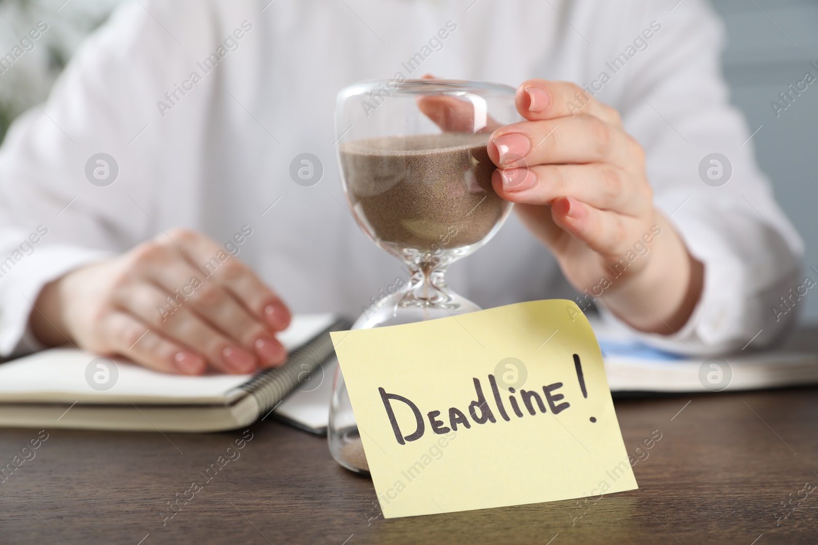 Deadline. Woman with hourglass and notebooks at wooden table in office, closeup Photo of Deadline. Woman with hourglass and notebooks at wooden table in office, closeup