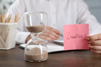 Photo of Woman holding sticky note with word Deadline at wooden table in office, closeup