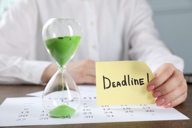 Photo of Woman holding sticky note with word Deadline at wooden table in office, closeup