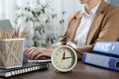 Photo of Deadline. Woman with laptop at wooden table in office, focus on alarm clock