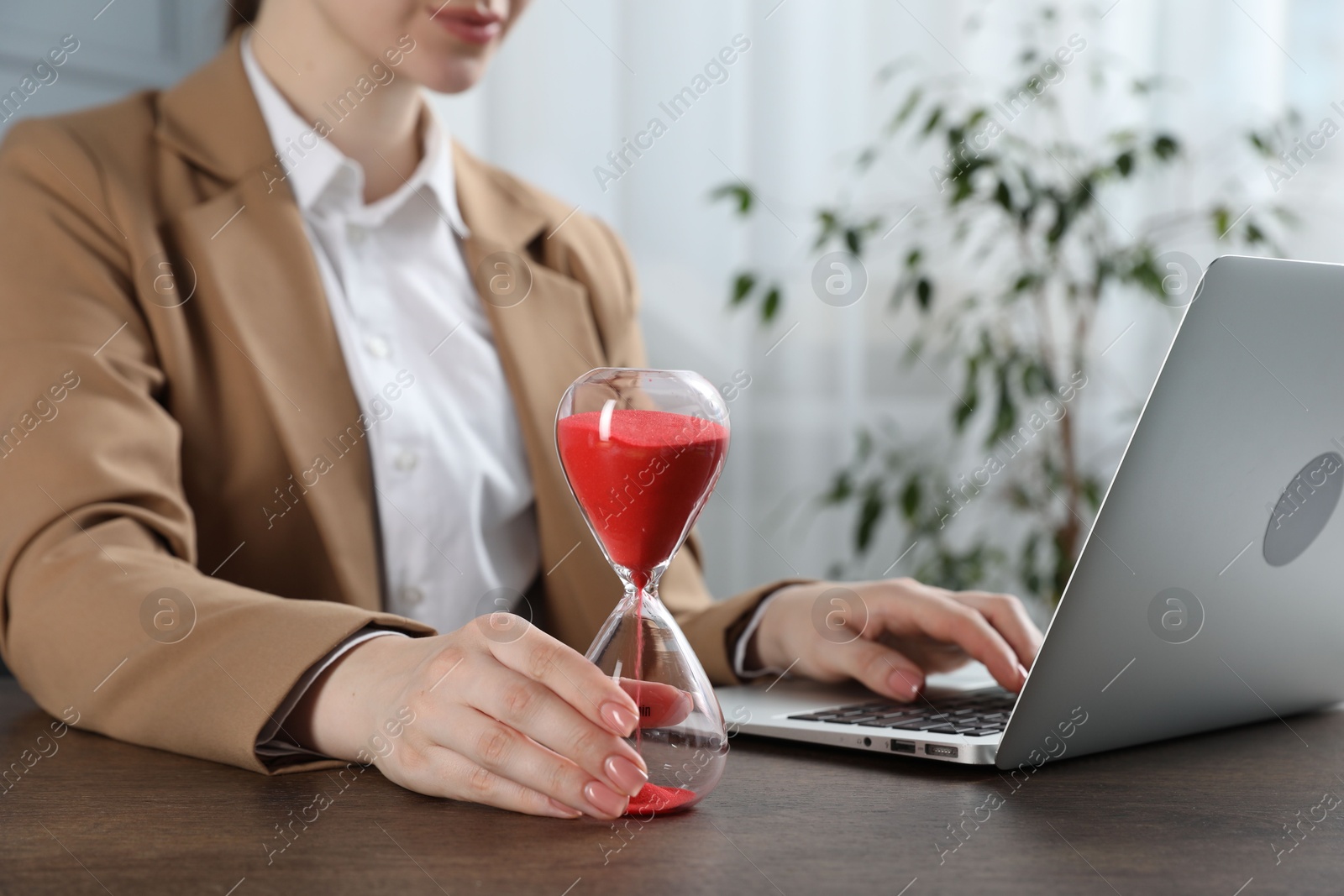 Deadline. Woman with hourglass and laptop working at wooden table in office, closeup Photo of Deadline. Woman with hourglass and laptop working at wooden table in office, closeup