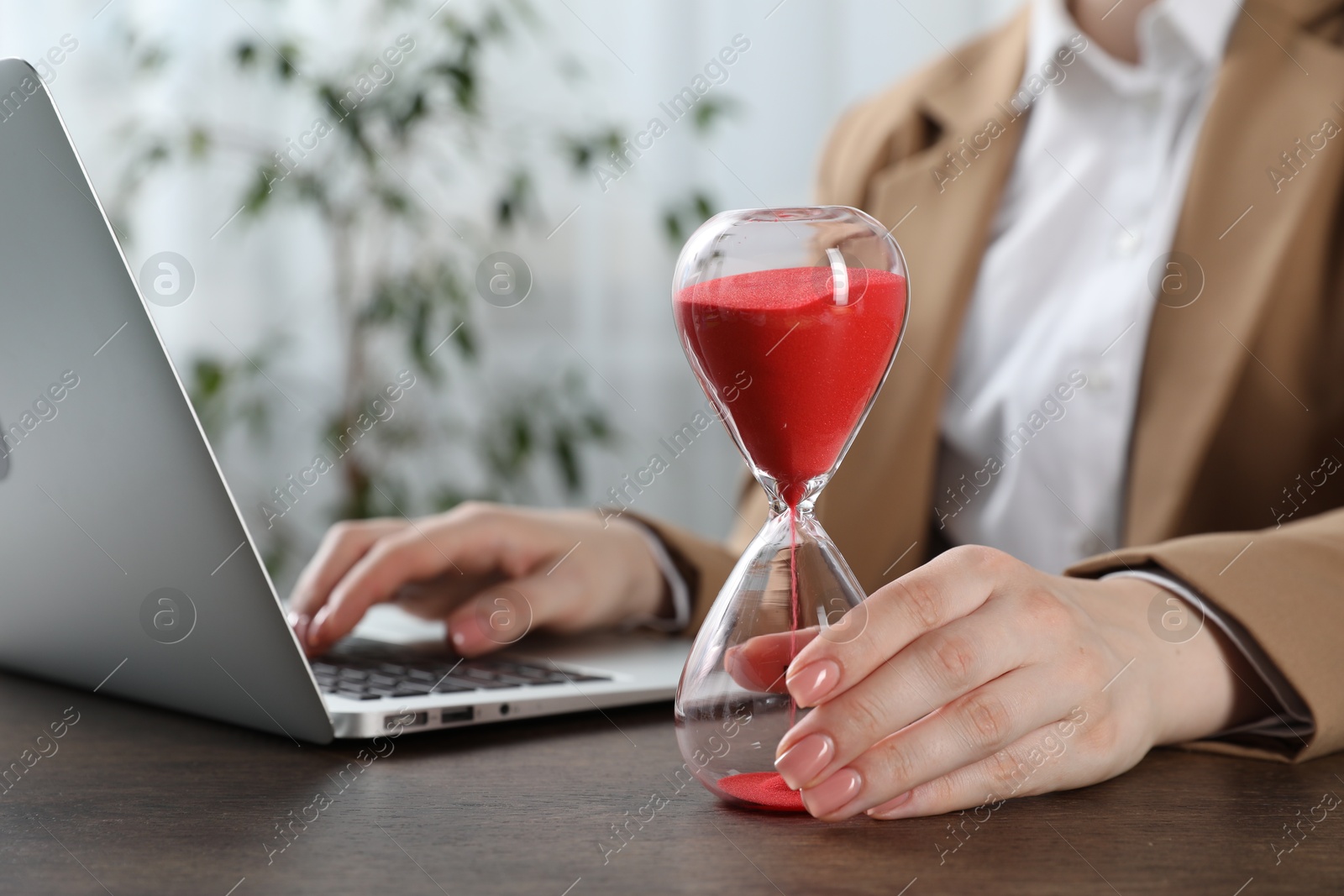 Deadline. Woman with hourglass and laptop working at wooden table in office, closeup Photo of Deadline. Woman with hourglass and laptop working at wooden table in office, closeup