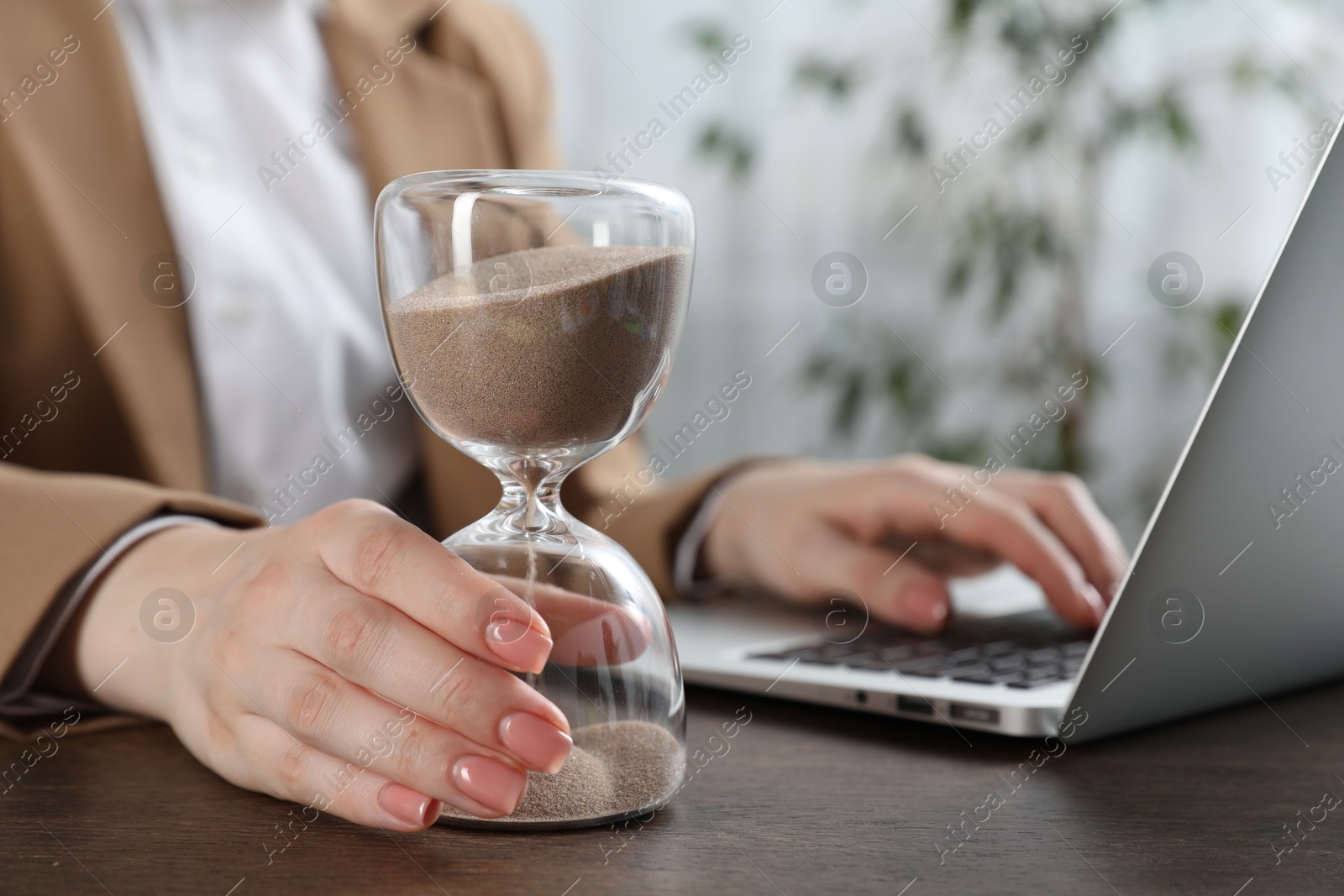 Deadline. Woman with hourglass and laptop working at wooden table in office, closeup Photo of Deadline. Woman with hourglass and laptop working at wooden table in office, closeup