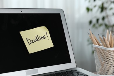 Photo of Sticky note with word Deadline attached to laptop indoors