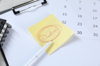 Photo of Sticky note with word Deadline, clipboard, calendar, pen and notebook on table, closeup