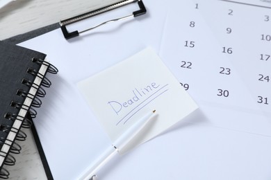 Photo of Sticky note with word Deadline, clipboard, calendar, pen and notebook on table, closeup