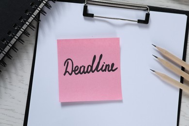Photo of Sticky note with word Deadline, clipboard, notebook and pencils on white wooden table, top view
