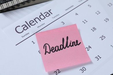 Photo of Sticky note with word Deadline and calendar on table, closeup