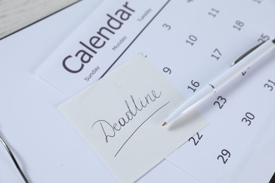 Photo of Sticky note with word Deadline, calendar, clipboard and pen on table, closeup