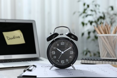 Photo of Deadline. Alarm clock, laptop, stationery and calendar on table indoors