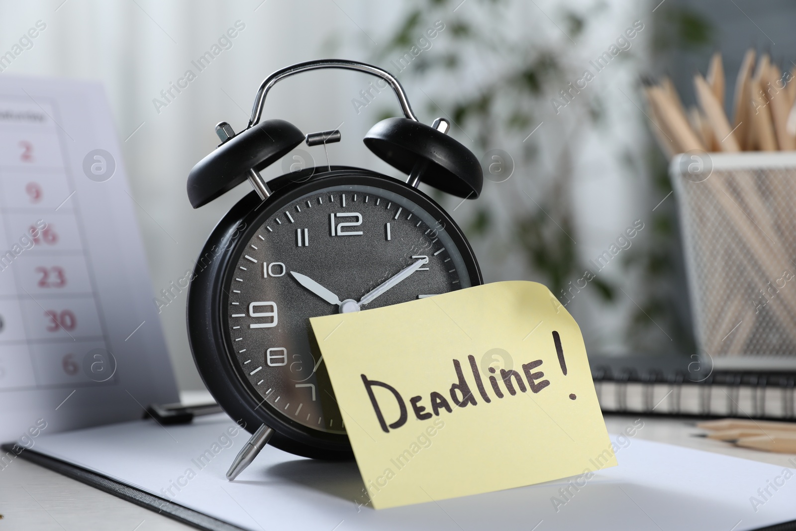 Sticky note with word Deadline, alarm clock, stationery and calendar on table indoors, closeup Photo of Sticky note with word Deadline, alarm clock, stationery and calendar on table indoors, closeup