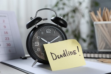 Photo of Sticky note with word Deadline, alarm clock, stationery and calendar on table indoors, closeup