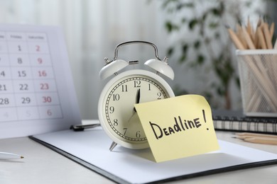 Photo of Sticky note with word Deadline, alarm clock, stationery and calendar on table indoors