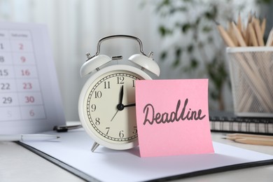 Photo of Sticky note with word Deadline, alarm clock, stationery and calendar on table indoors
