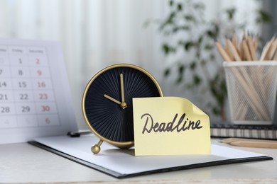 Photo of Sticky note with word Deadline, alarm clock, stationery and calendar on table indoors