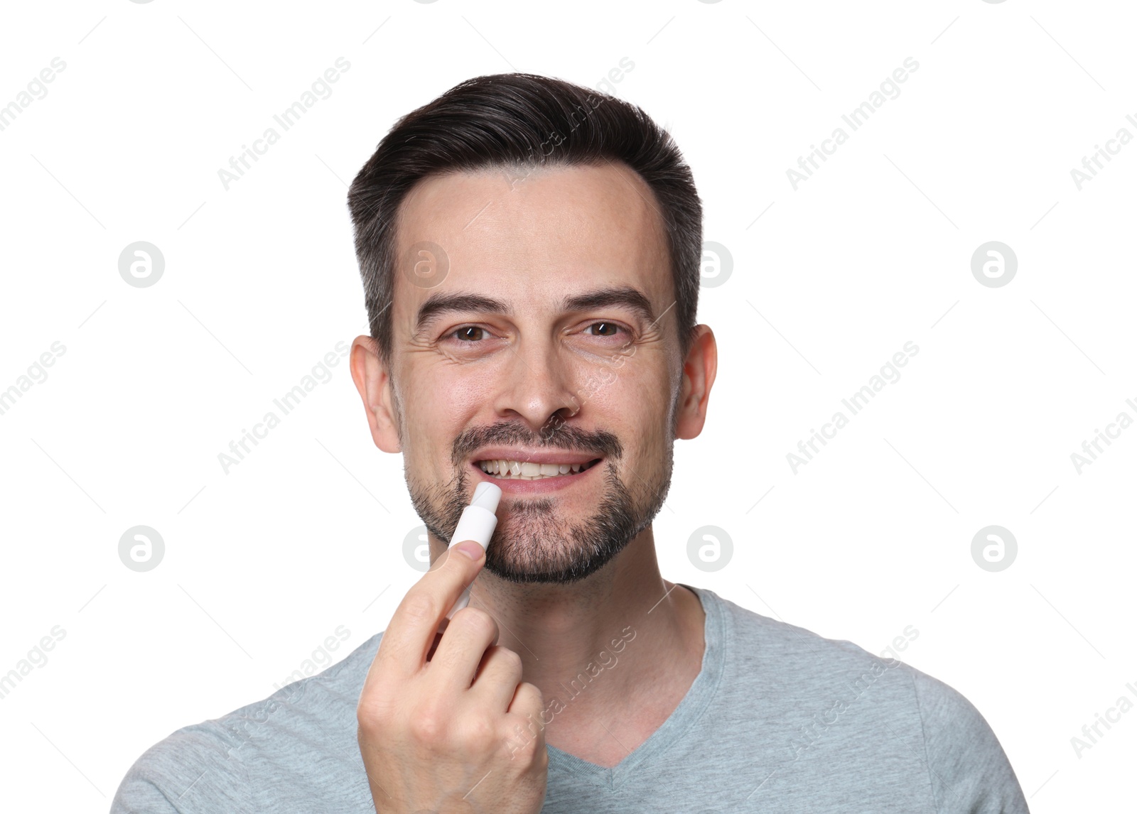 Photo of Smiling man applying lip balm onto his lips on white background