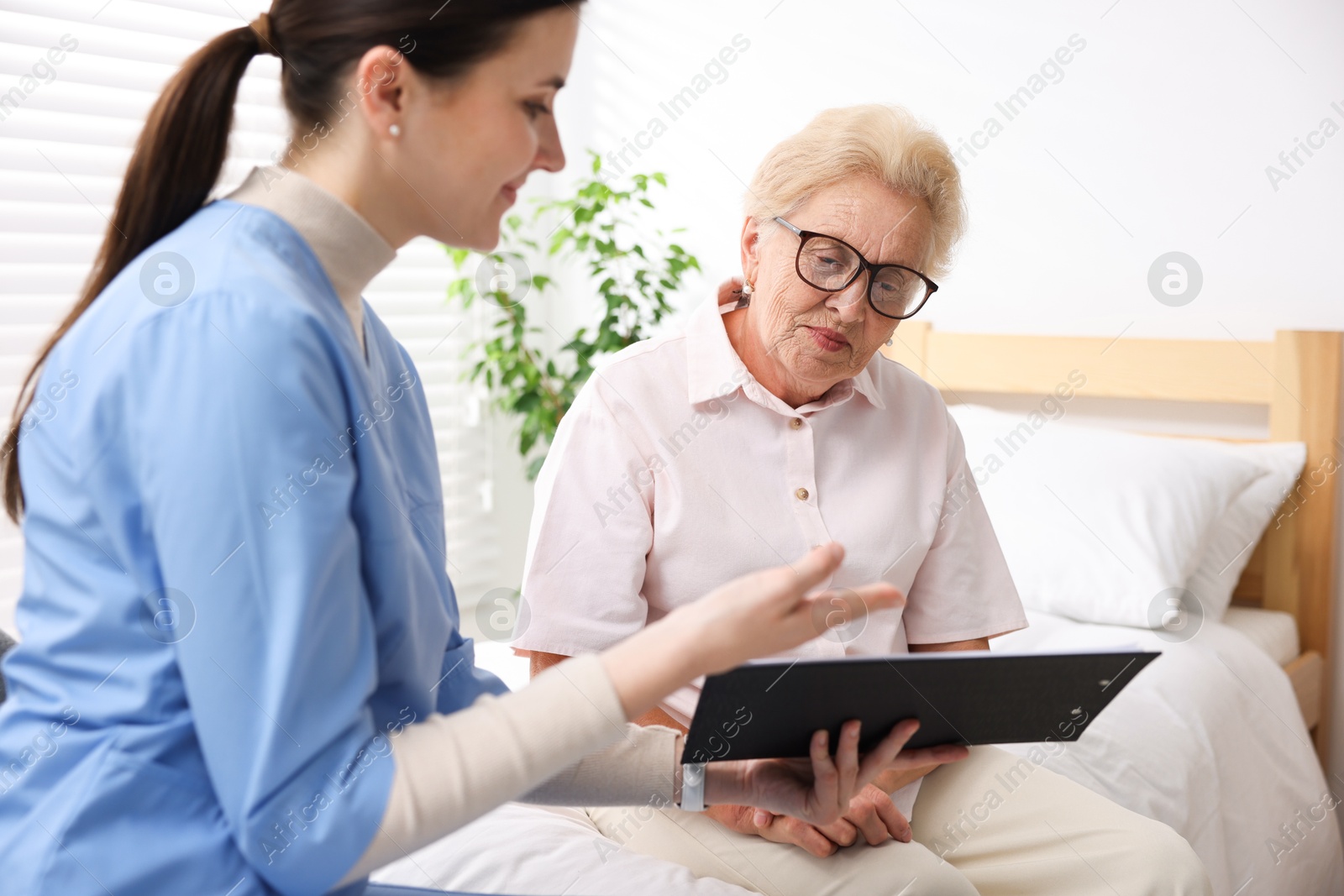 Photo of Nurse with clipboard examining senior woman indoors. Home health care service