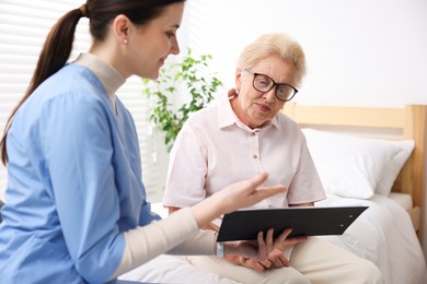 Photo of Nurse with clipboard examining senior woman indoors. Home health care service