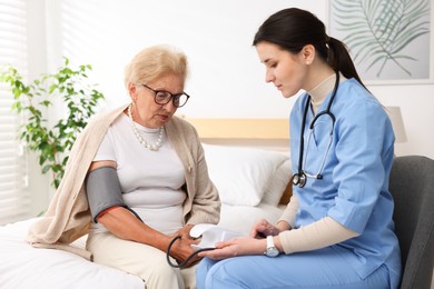 Photo of Nurse measuring patient's blood pressure indoors. Home health care service