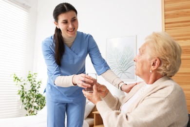 Photo of Nurse giving water to senior woman on sofa indoors. Home health care service