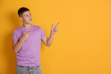 Photo of Teenage boy pointing at something on orange background, space for text